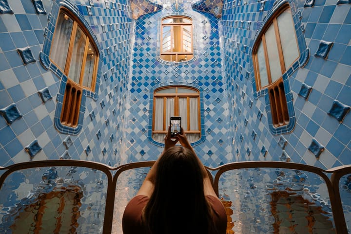 Person taking a photo with a smartphone inside a blue tiled architectural interior with arched windows